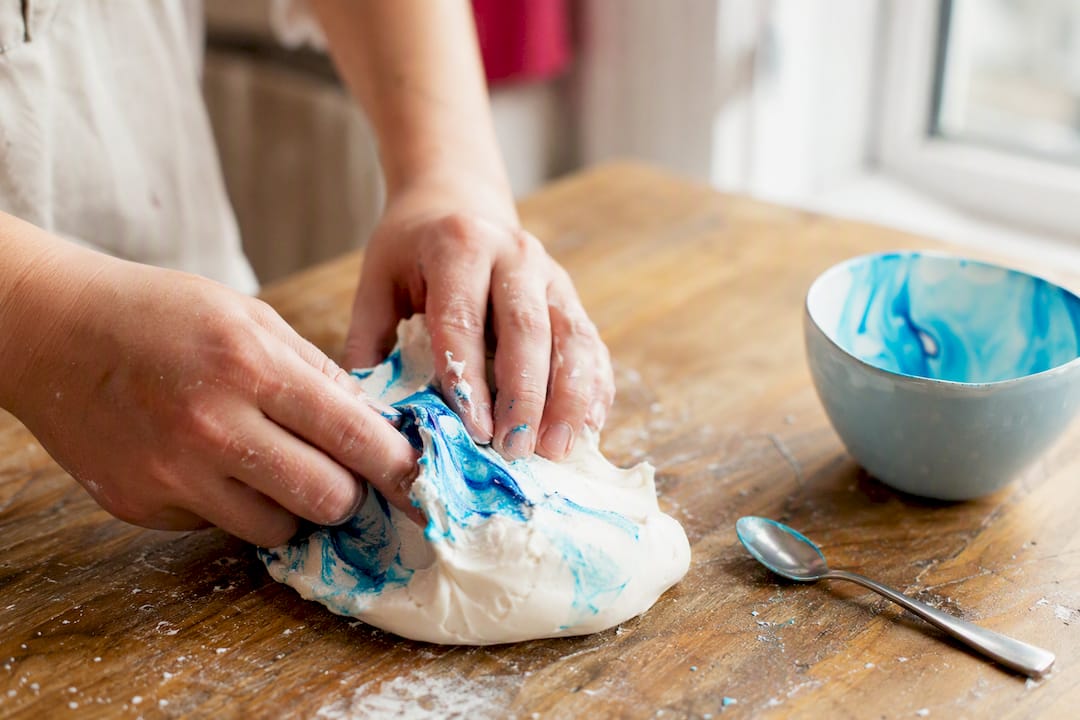 Hände, die Gel-Farbe in weiße Zuckerpaste einarbeiten