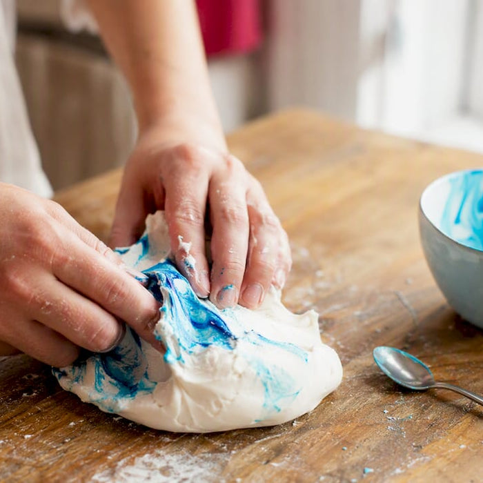 Hände, die Gel-Farbe in weiße Zuckerpaste einarbeiten