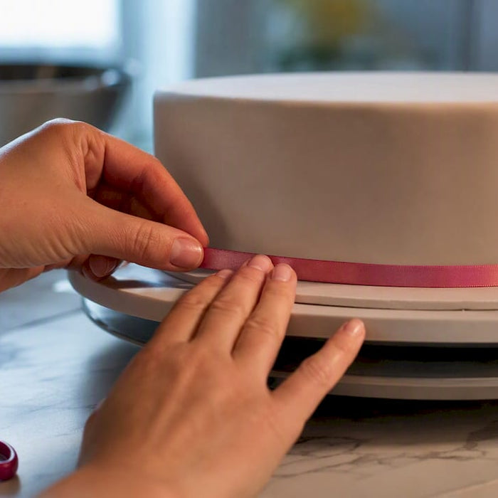 Hände befestigen ein Satinband am Rand der Fondant-Torte